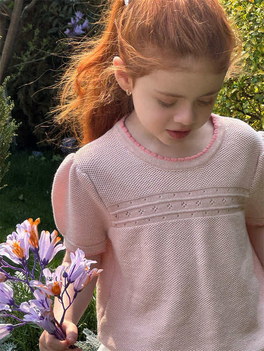 Young girl in a pink knit top holding flowers outdoors