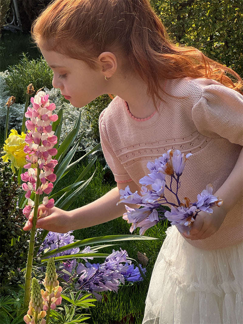 Young girl wearing a pink summer knit top holding flowers in a garden setting