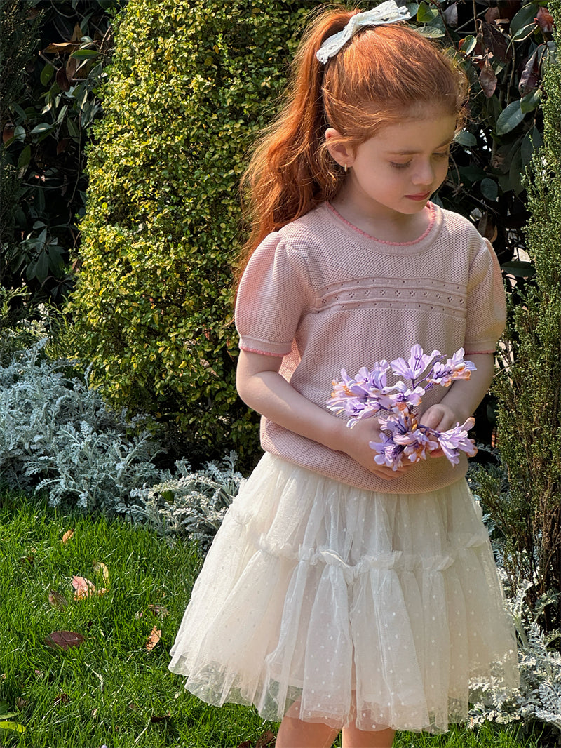 Young girl in a pink knit short sleevetop and white skirt holding flowers in a garden setting