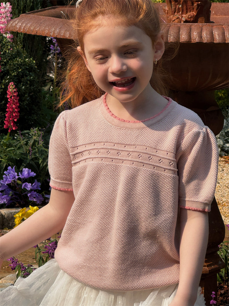 Young girl wearing a pink knitted short sleeve sweater in a garden setting