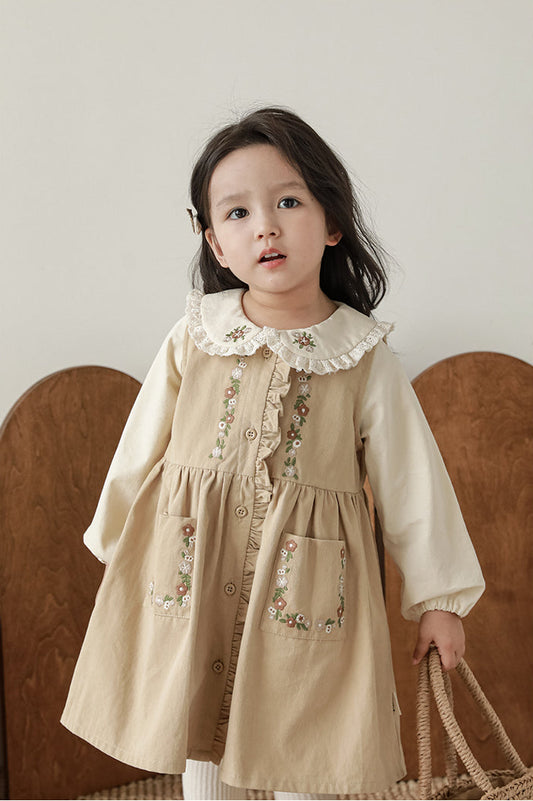 Young girl wearing a beige dress with floral embroidery against a neutral background