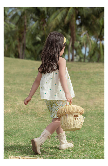 Young girl with cherry top walking on grass with a woven basket, surrounded by trees