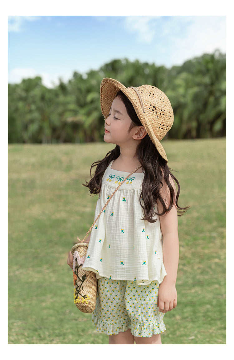 Young girl in muslin sleeveless top and bright shorts standing in a grassy field 