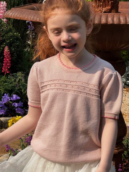 Young girl wearing a pink knitted short sleeve sweater in a garden setting